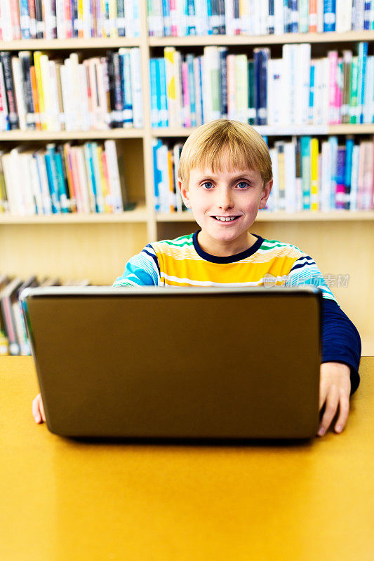 带着笔记本电脑微笑的金发男生在图书馆