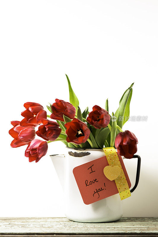 白色大水罐里放着红色郁金香，还有一张写着“我爱你”的卡片