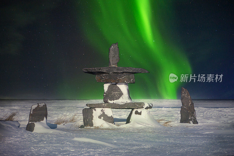 一种传统的石inukshuk，一种因纽特人的文化符号，被用作在遥远的北方指引旅行者的地标，表明他们走在正确的道路上。绿色的北极光在夜空中闪烁。