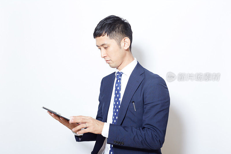 穿着西装的年轻日本商人摆弄着他的平板电脑