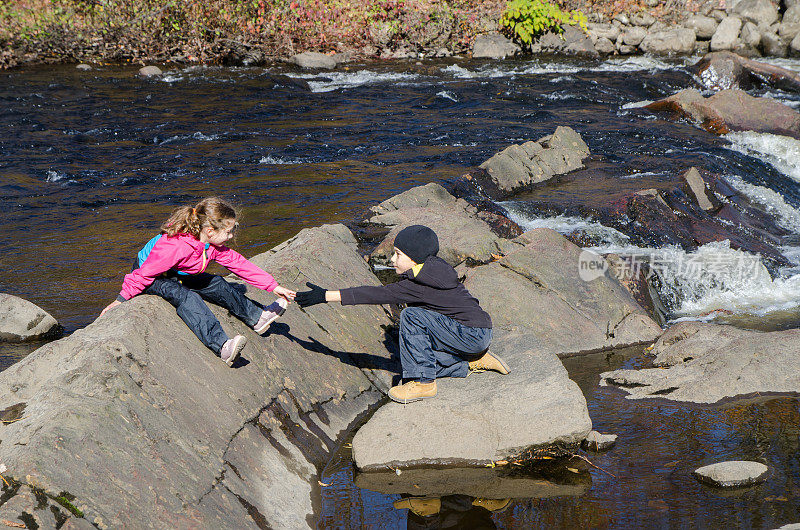 秋天的一天，魁北克市，一个男孩帮助他的妹妹在圣查尔斯河上的岩石上行走