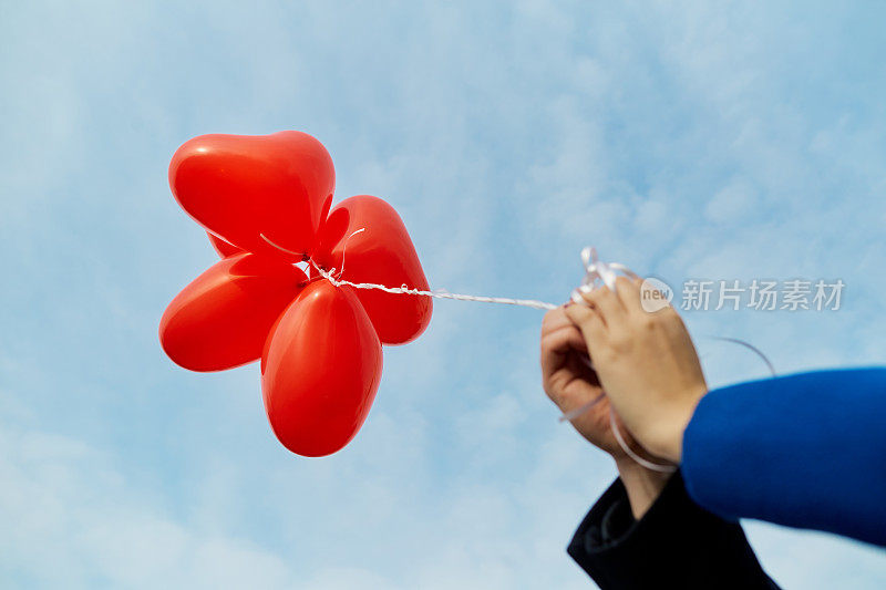 新婚夫妇的手拿着一个红心形状的气球。