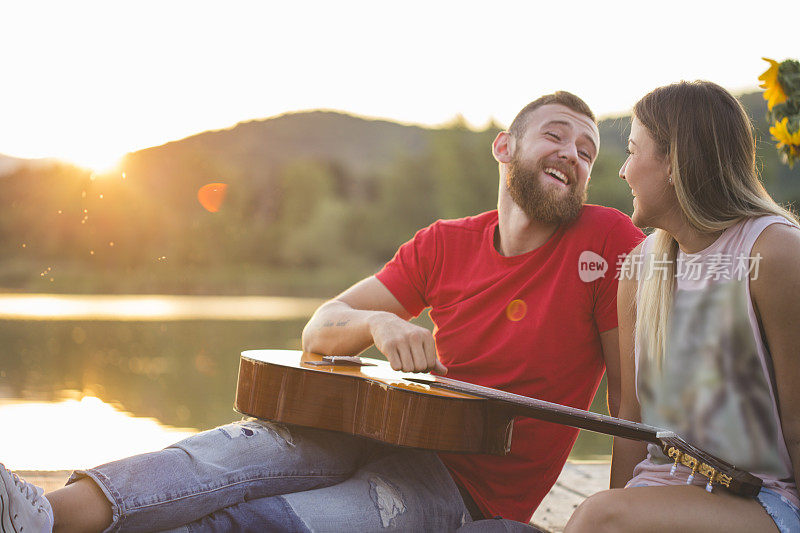 一对情侣在日落码头弹吉他快乐地在一起