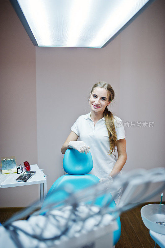 好看的女牙医摆姿势在一个现代装备良好的橱柜白大褂。