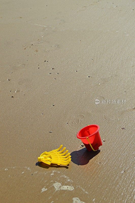 一个黄色的塑料耙和一个红色的塑料桶或沙桶在沙滩上