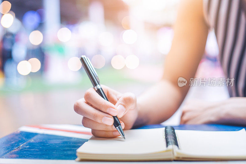 在木桌上用钢笔在笔记本上写字的女人的手。