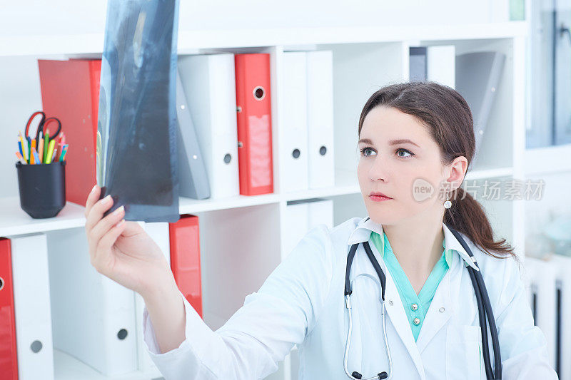 年轻女医生或实习生站在她的办公室看肺部x光图像。放射学、医疗保健、医疗服务或教育概念。