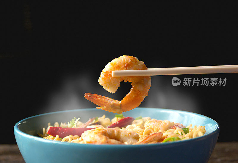 用筷子手捡虾与方便面与烟孤立在黑色背景。