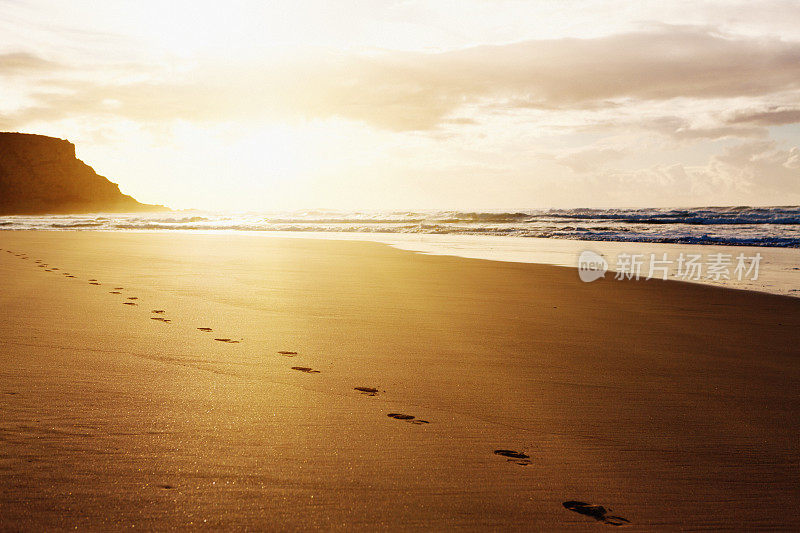 日出或日落凸显一个孤独的海滩漫步者的脚印