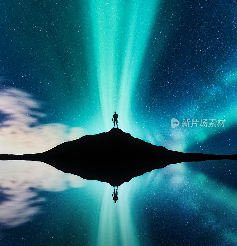 挪威的北极光和站在山上的男人的剪影。北极光和人类。星星和绿色的北极光。夜景与极光、湖水、天空倒影在水中。旅行。概念