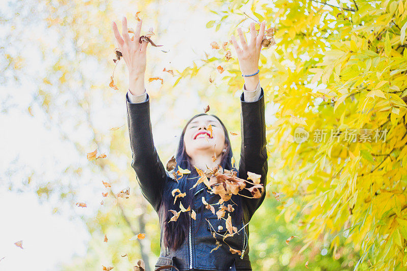 在秋天的公园里，女人把树叶抛向空中。