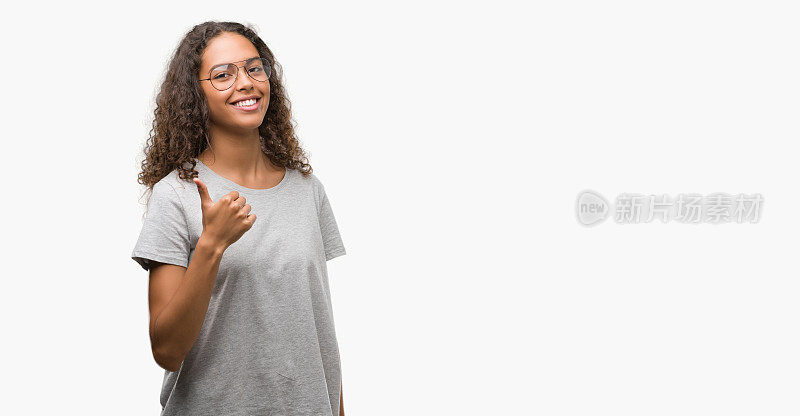 美丽的年轻西班牙妇女戴眼镜做快乐的拇指手势与手。赞许的表情看着镜头，表示成功。
