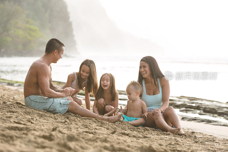 欧亚大陆的父母和他们的孩子在夏威夷海滩的沙滩上玩耍
