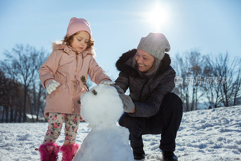 奶奶和孙女在冬天堆雪人