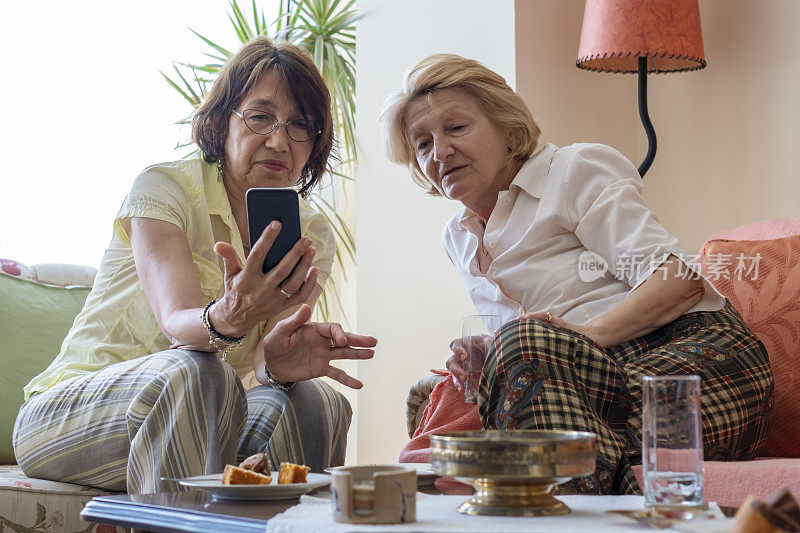两位资深女性在家里用手机聊天