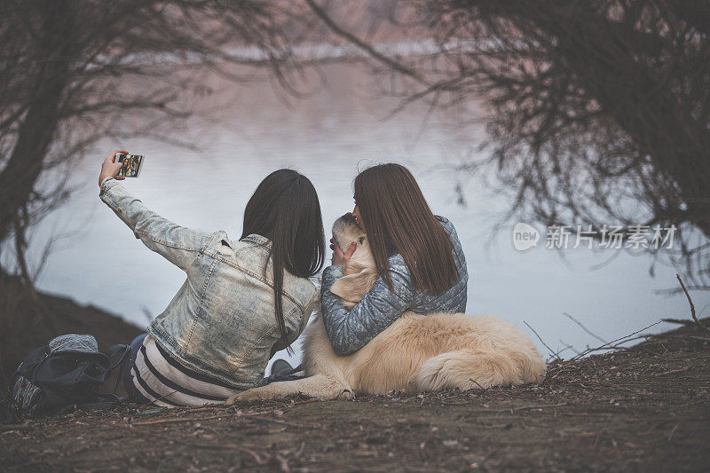 两个年轻的女人在河边自拍和他们的狗