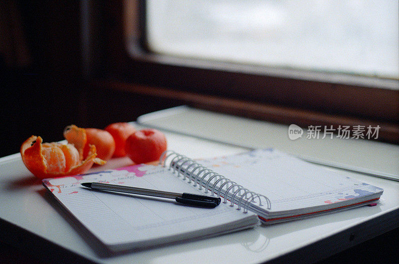 火车车厢的桌子上放着个人记事本，里面有水瓶和橘子