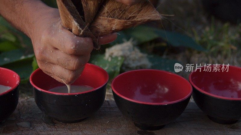 在南太平洋瓦努阿图的一个热带岛屿上，一名当地黑人青年正在准备卡瓦果汁饮料，他把它挤成小杯