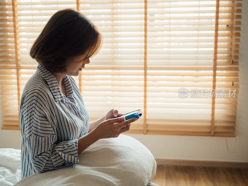 年轻的亚洲女人拿着药瓶，在卧室里讲手机