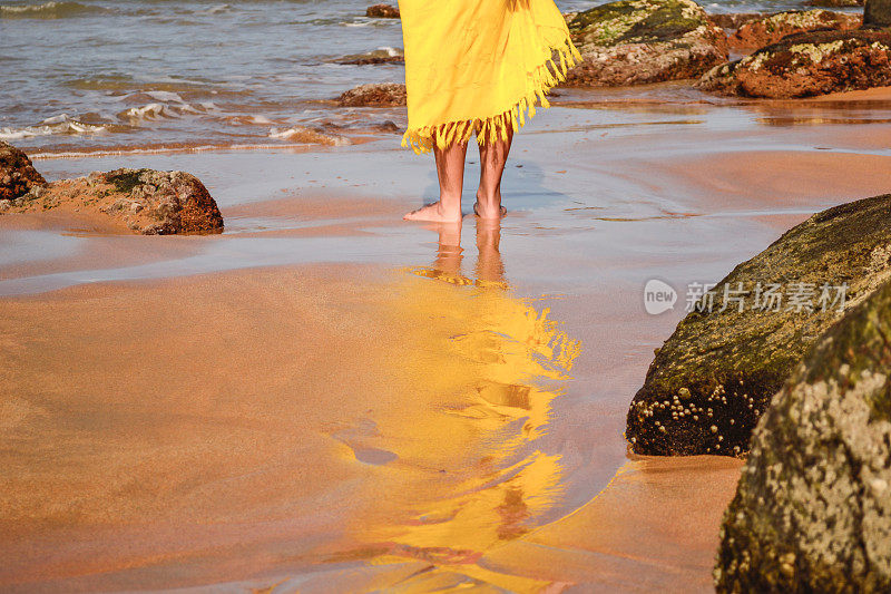 沙滩上穿着黄色纱笼的女人的腿