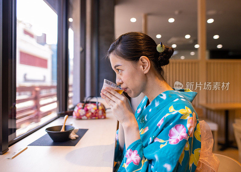 年轻女子在yukata喝冷茶后吃糖果在日本风格的咖啡馆