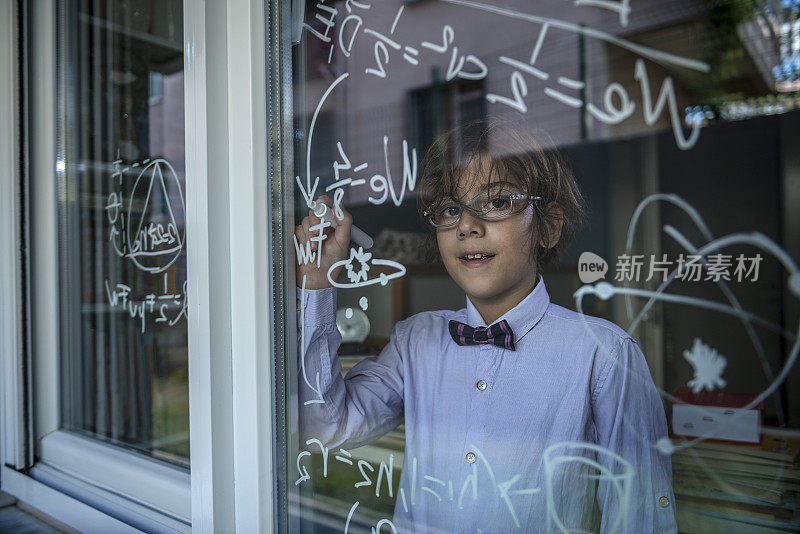 天才男孩在窗户上写公式。