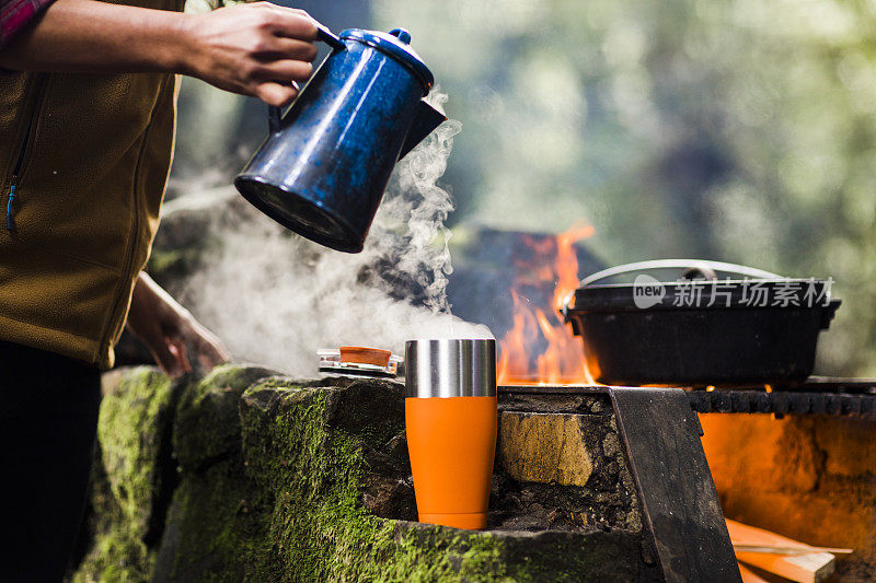 在树林里露营时，早上用壶倒咖啡