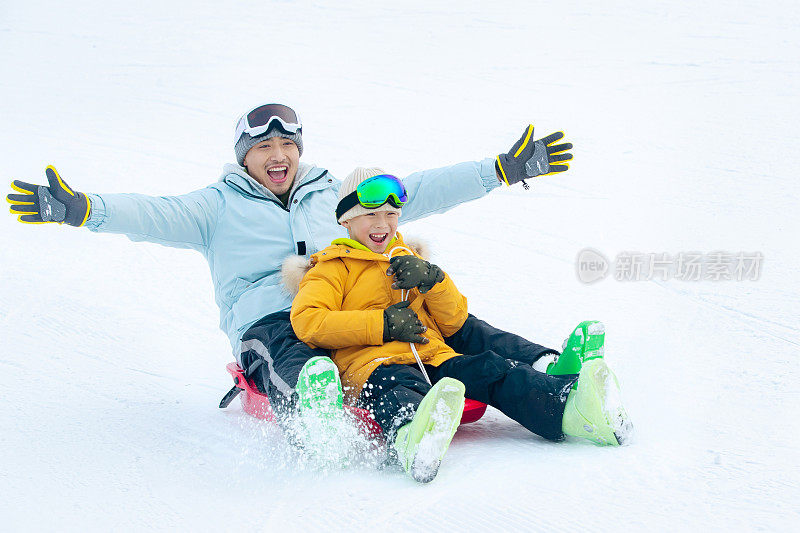 快乐父子坐着雪上滑板滑雪