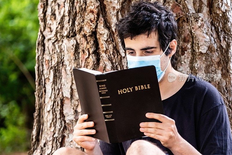 一个戴着医用口罩读圣经的年轻人