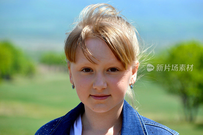 肖像10岁的俄罗斯金发女孩微笑在绿色的田野背景。可爱的脸，看着镜头