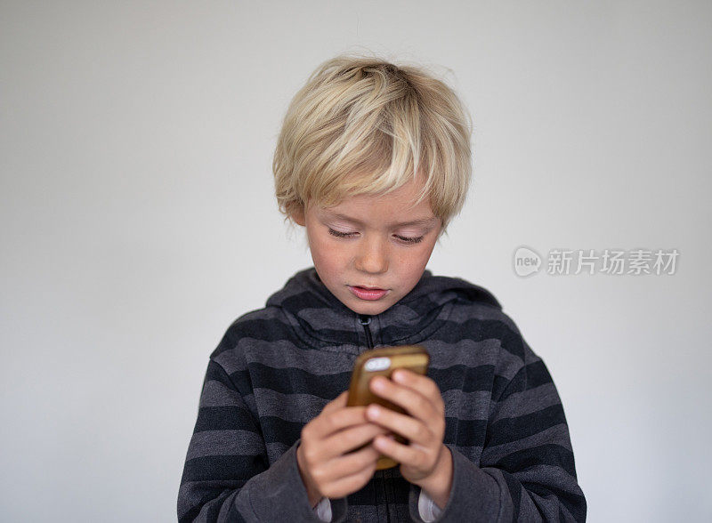 一个小男孩在一个白色屏幕前摆姿势。他们手里拿着一个手机
