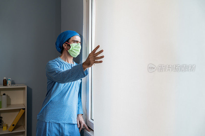 冠状病毒隔离期间戴口罩的成年男子站在窗边