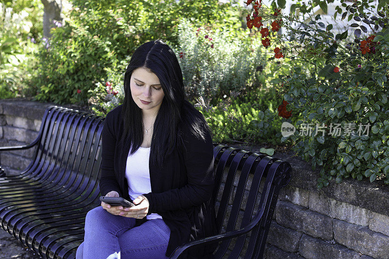 美女坐在公园长椅上玩手机
