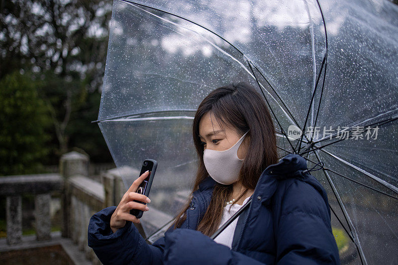 一名年轻女子戴着防护面罩在下雨天在公园拍照