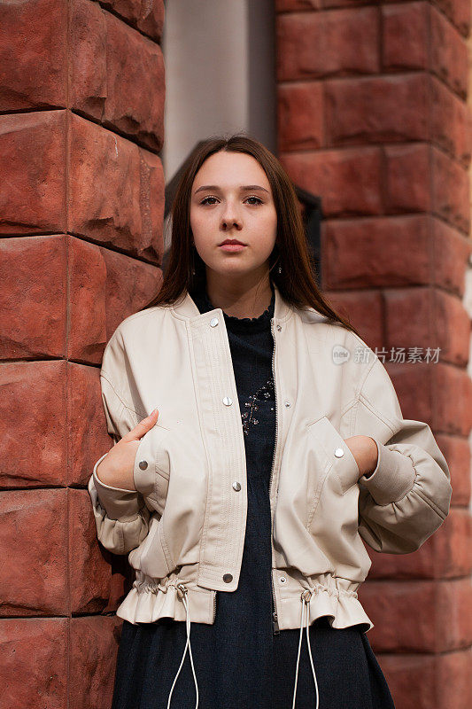 年轻女子站在一堵砖墙旁边