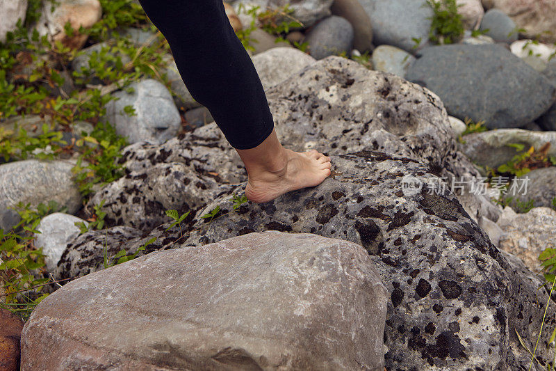 一个女人光着脚走在石头上。裸露的女性脚特写。