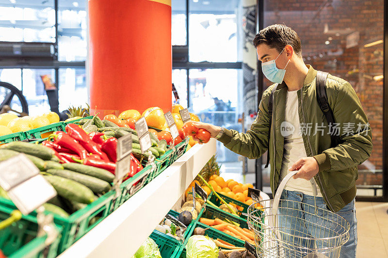 一名戴着医用口罩的男子在商店里采摘时令水果。冠状病毒大流行。