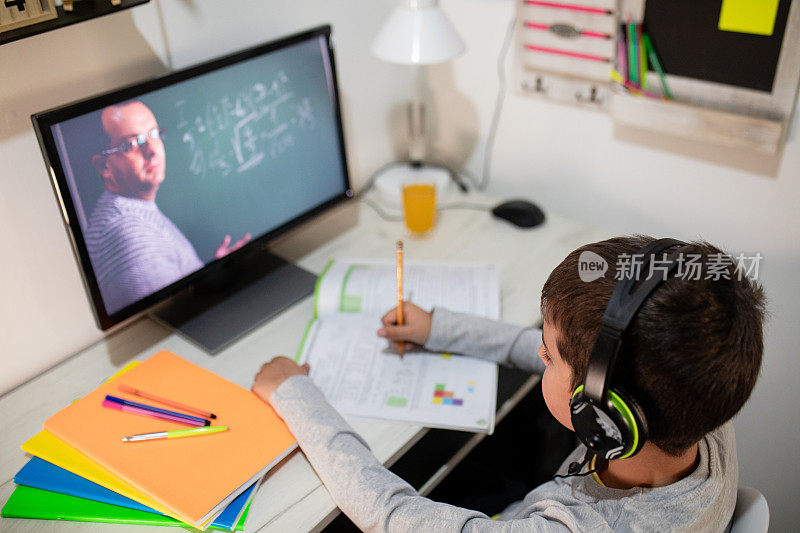 远程学习中，一个男孩戴着耳机坐在家里的桌子旁。理念线上教育、家庭教育、科技、学校