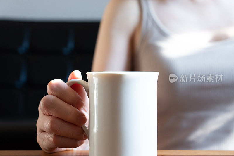 一个女人在她的房子的客厅里喝着咖啡放松。