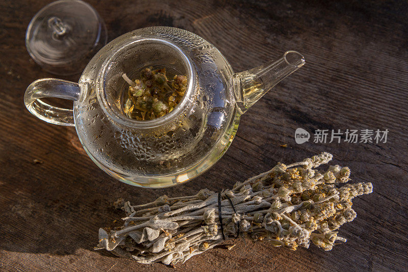 透明茶壶与泡制的绿色花草茶在木材背景。