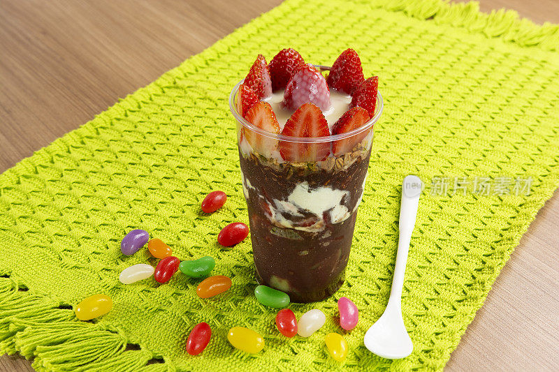 巴西巴西莓杯与草莓顶，炼乳和彩色果冻豆在绿色背景，巴西莓冷冻