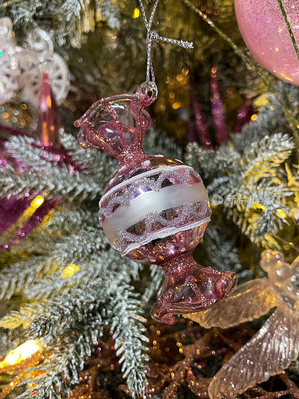 个性形象，甜美的粉色糖果包装纸点缀在人造圣诞树的树枝上，云杉针上覆盖着人造雪花喷雾，模糊的白色精灵灯光背景