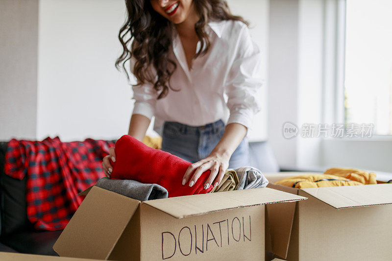 在她的房间里，一个女人拿着捐赠箱的衣服，捐赠的概念