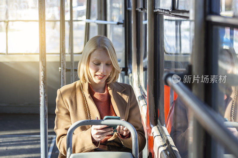 现代微笑可爱的女人坐在公共汽车上。微笑着看向别处。公共汽车旅行。一个女人在公车上用手机。电车。短信,信息。在公共交通上拿着手机的女人