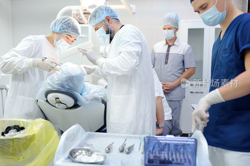 牙科手术中的外科医生和护士。手术室里被麻醉的病人。在诊所安装种植牙。