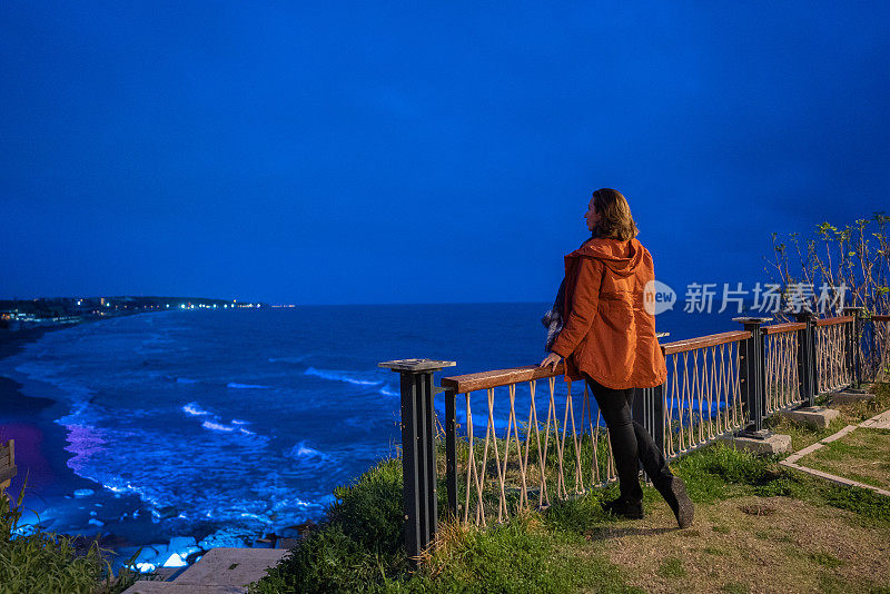 成熟的女人在黄昏的海岸线上看海景