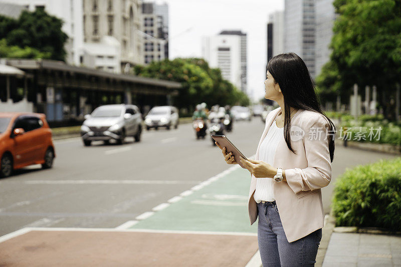 亚洲成年人在街上拿着平板电脑抬头看