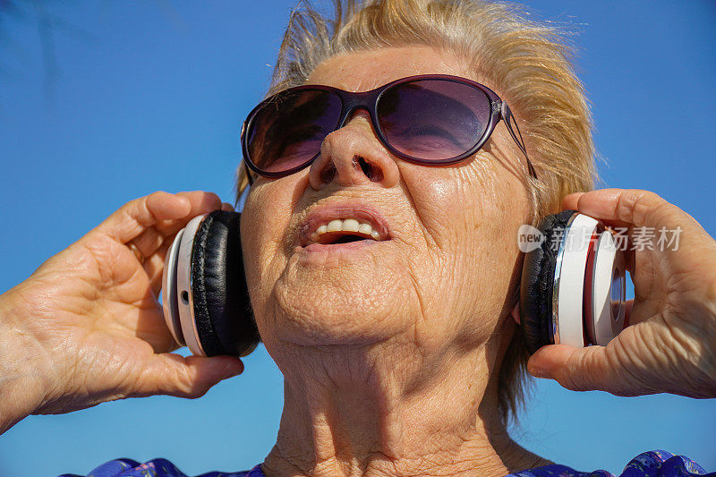 老妇人在公园里戴着耳机唱歌。治疗老年痴呆症