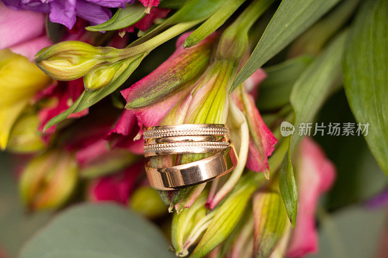 新娘和新郎的结婚金戒指躺在新娘的一束花的背景，金戒指