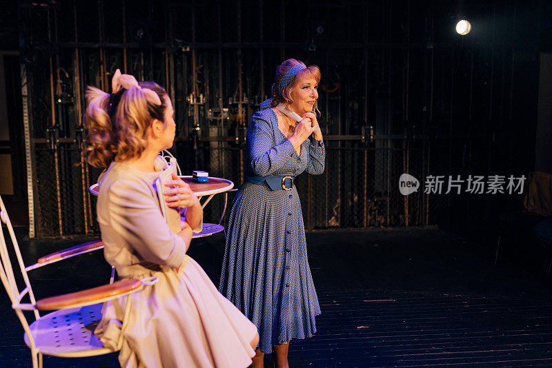 两位女艺术家站在剧院的舞台上，在夜间排练戏剧的文本